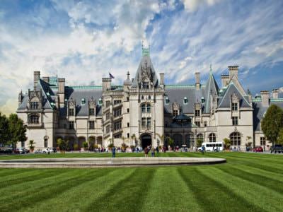 Grand French chateau style Biltmore mansion, several steep roof peaks, huge green front lawn, blue skies with white clouds