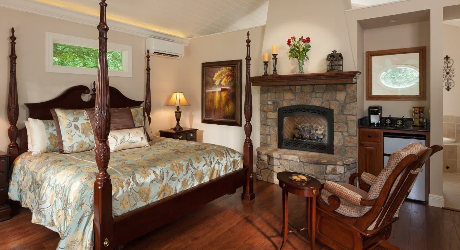 Large bedroom with four poster bed, stone fireplace, mini kitchenette and rocking chair