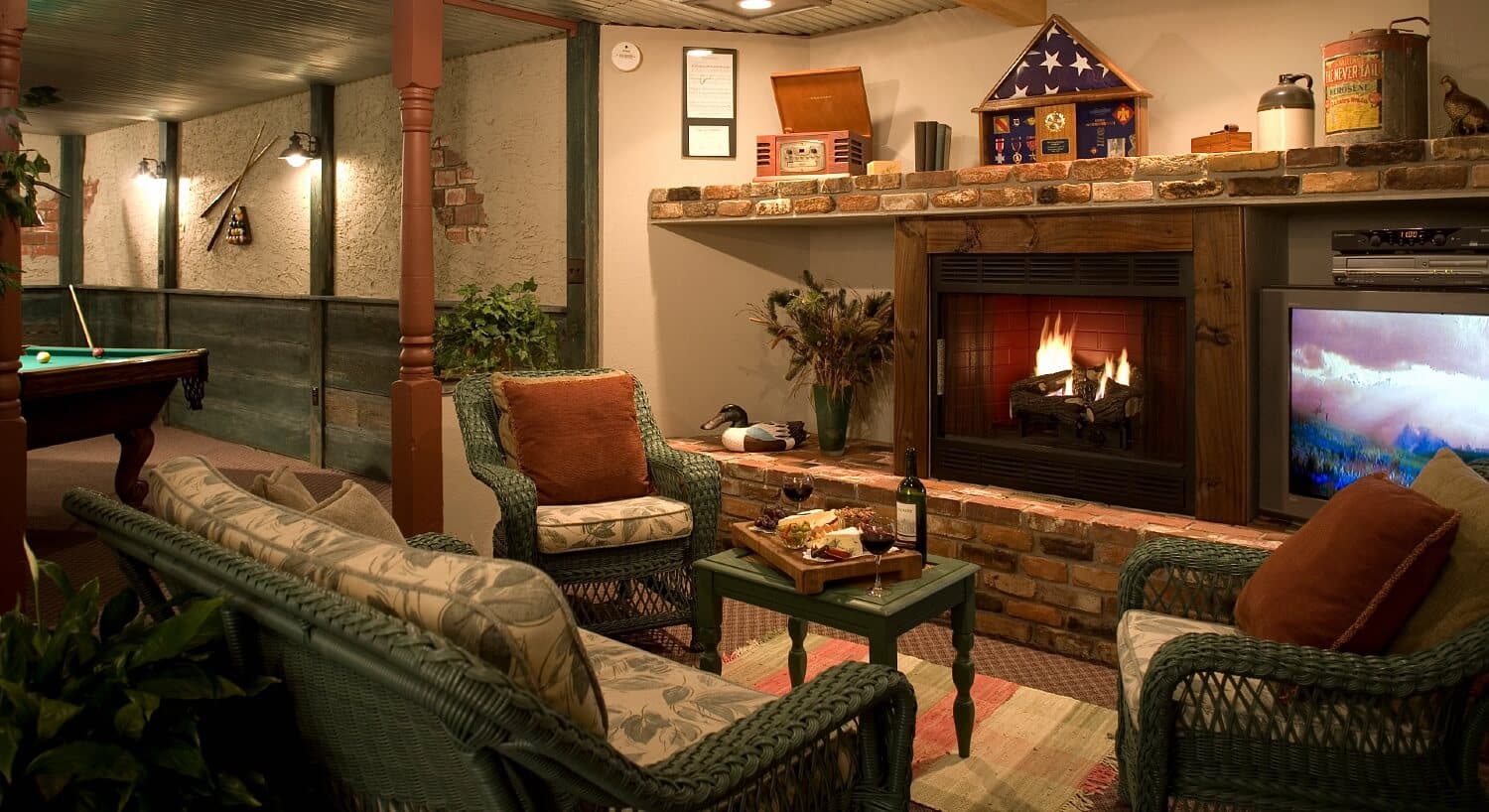 Basement room of a home couch and chairs in front of a roaring fireplace, TV and a side room with a pool table