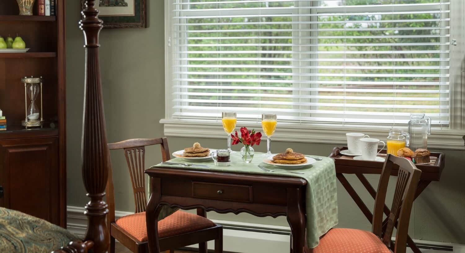 Table set for two with plates of pancakes, glasses of orange juice and side tray with coffee and muffins