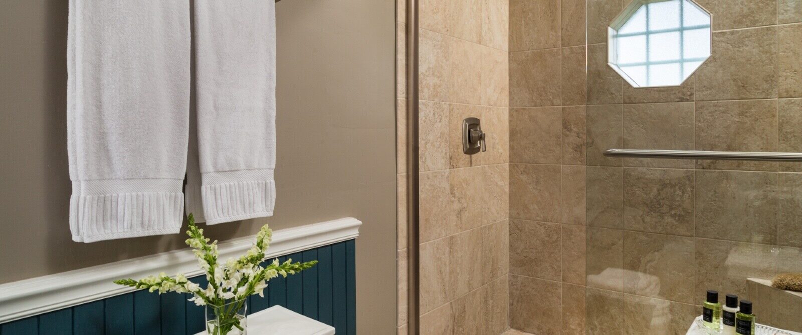 Bathroom with large tiled stand up shower with glass doors and white towels hanging on the wall