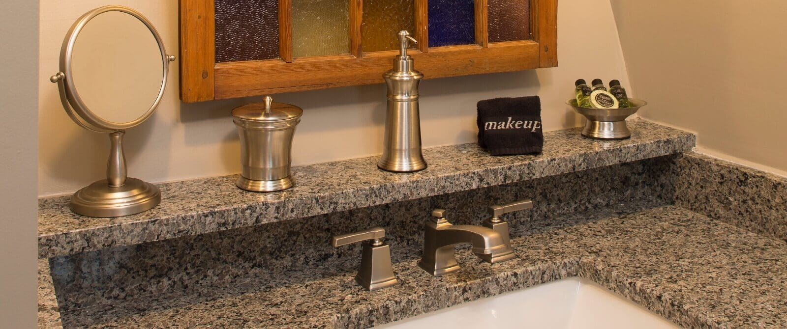 Sink vanity with granite counter tops, stainless steel accents and decorative wood mirror above