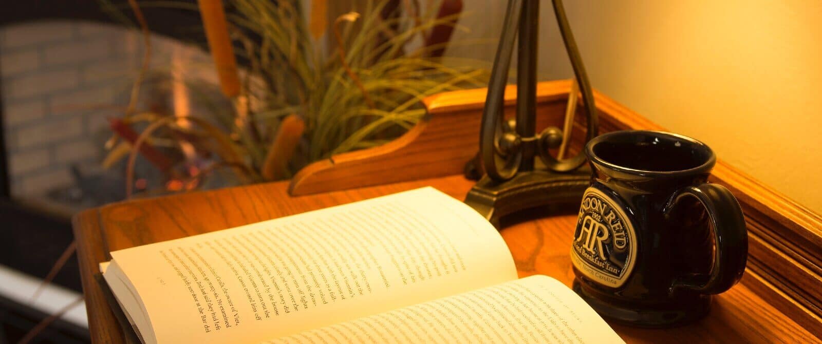 Writing desk with lamp and open book next to a ceramic coffee mug