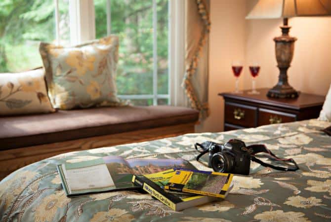 Close up view of bed topped with camera and guide books and a window with window seat in background