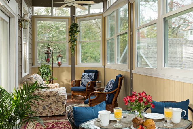 Creamy yellow sunroom with lots of windows, ceiling fans, upholstered furniture and dining table and chairs