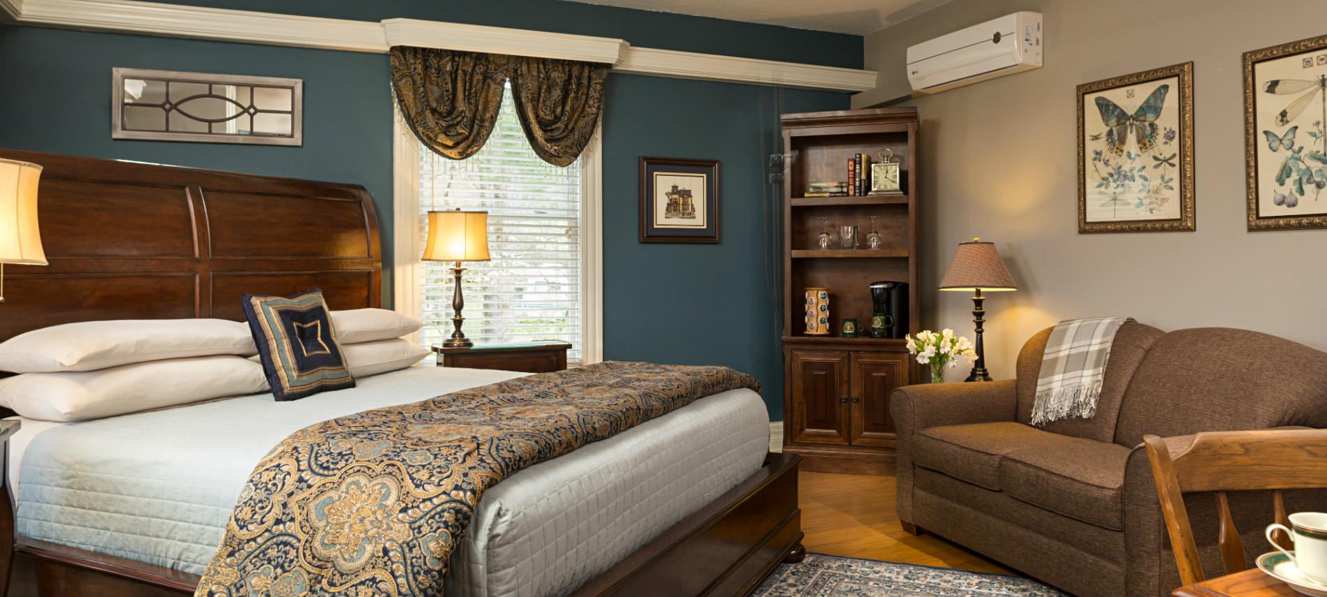 Elegant beige and navy room with wood floors, wood sleigh bed with blue and gold bedding, loveseat and window