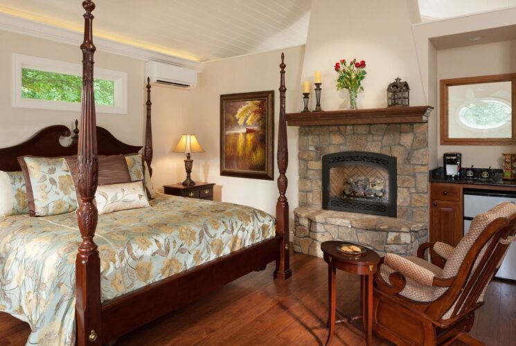 Large bedroom with four poster bed, stone fireplace, mini kitchenette and rocking chair