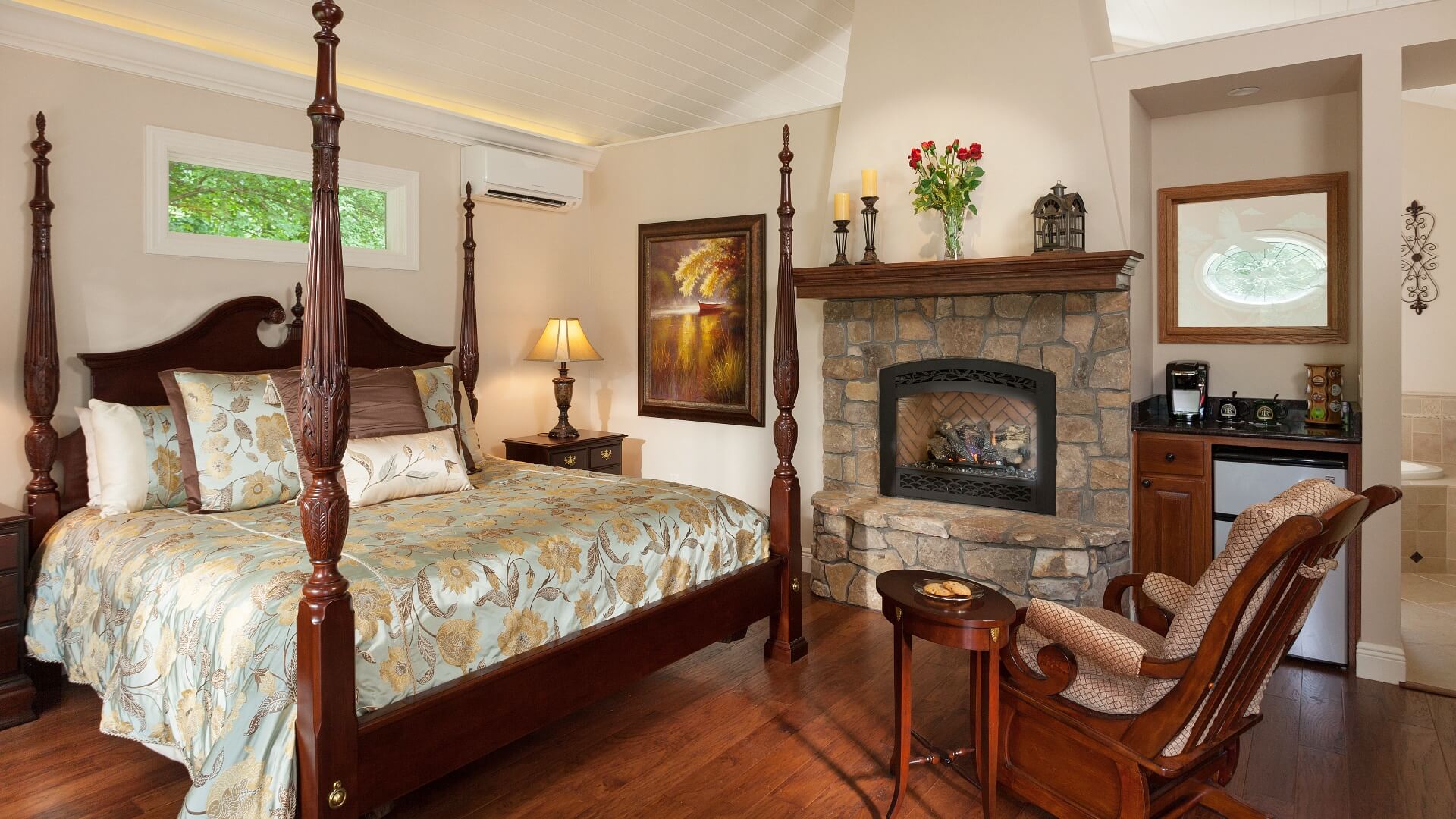 Large bedroom with four poster bed, stone fireplace, mini kitchenette and rocking chair