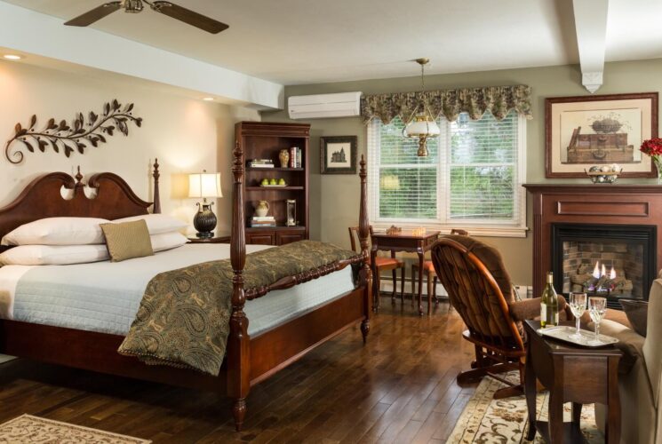 Spacious bedroom with king four poster bed, sitting table an two chairs in front of a fireplace