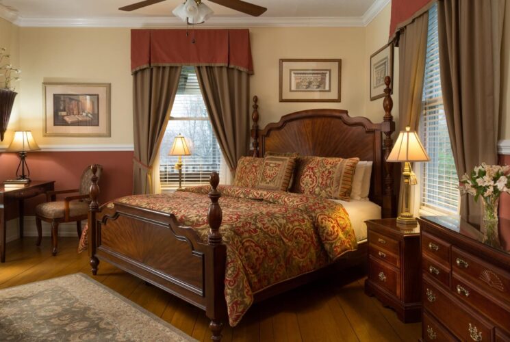 Romantic bedroom with hues of rust and brown, king bed, writing desk and chair and large windows with elegant drapes