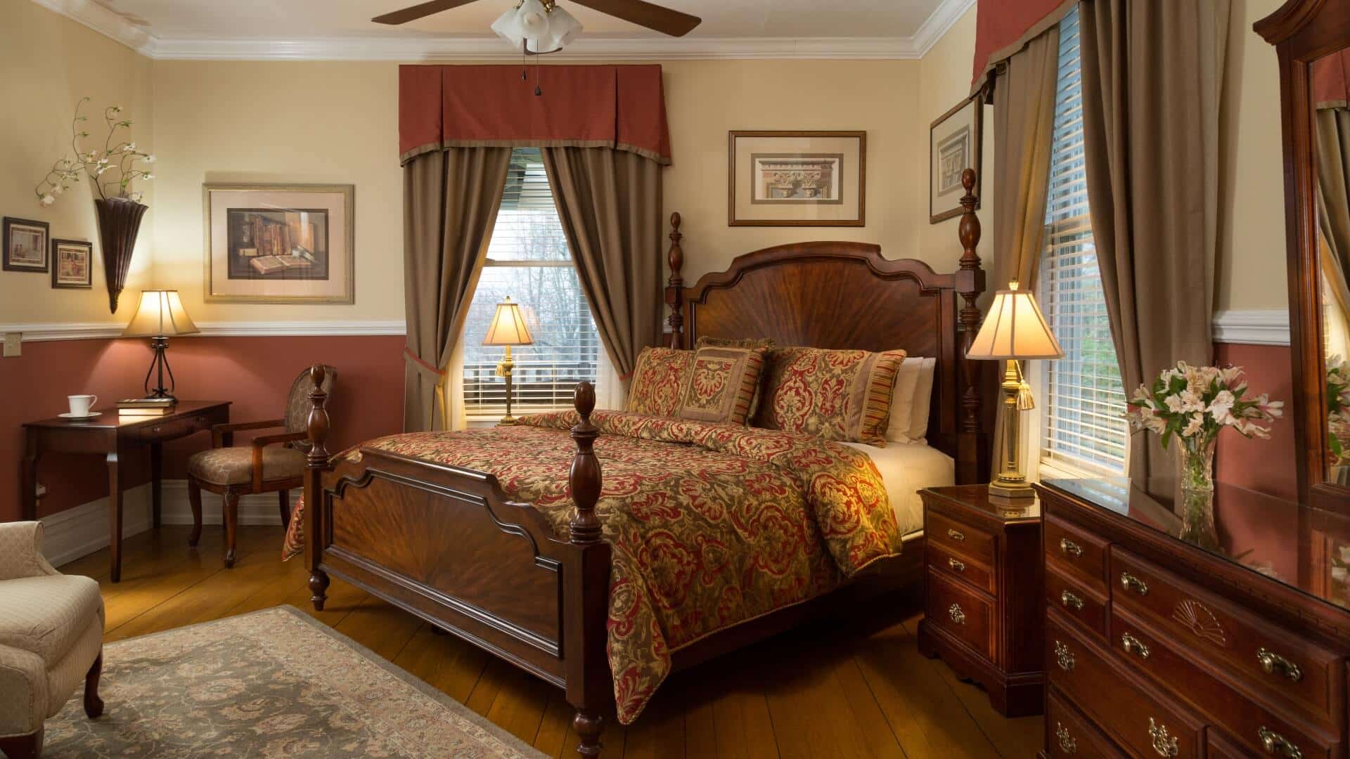 Romantic bedroom with hues of rust and brown, king bed, writing desk and chair and large windows with elegant drapes