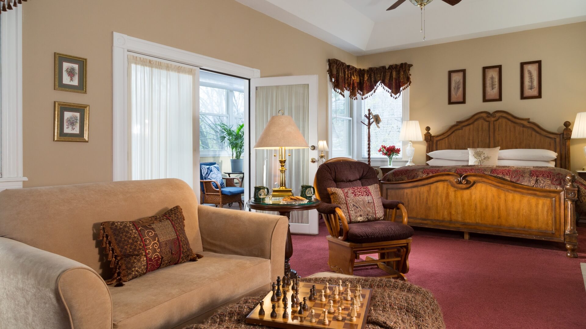 Elegant bedroom with king bed, couch, table and French doors open to a bright sitting room with windows