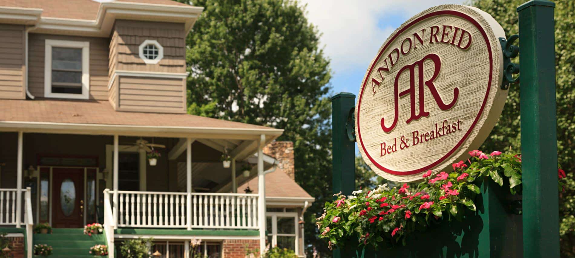 Andon Reid Bed & Breakfast sign hanging on green post with pink flowers, view of brown sided B&B in the background