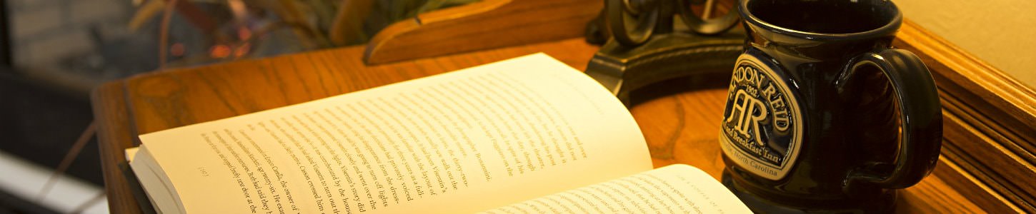 Close up view of an open book on a desk with a lamp and Andon Reid coffee mug