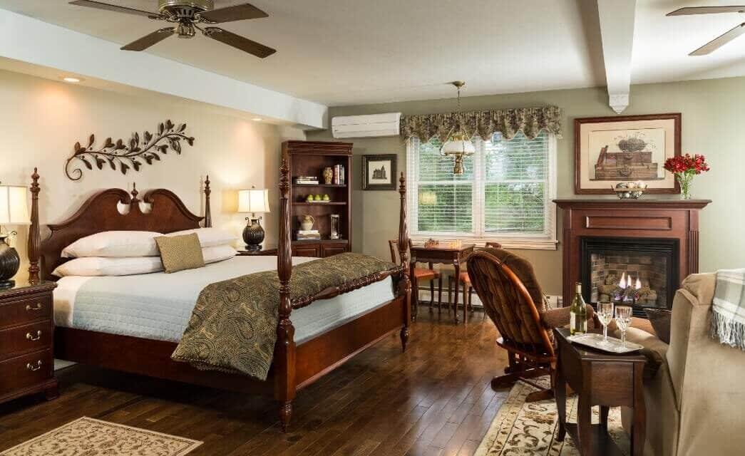 Spacious bedroom with king four poster bed, sitting table an two chairs in front of a fireplace