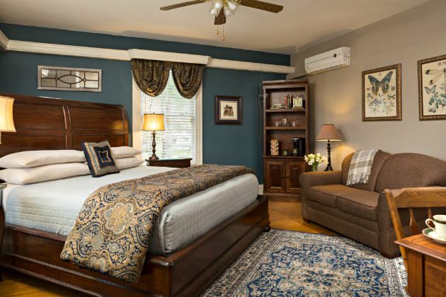 Elegant beige and navy room with wood floors, wood sleigh bed with blue and gold bedding, loveseat and window
