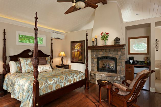 Charming guest room with four poster bed, wood floors, stone fireplace, rocking chair and ceiling fan