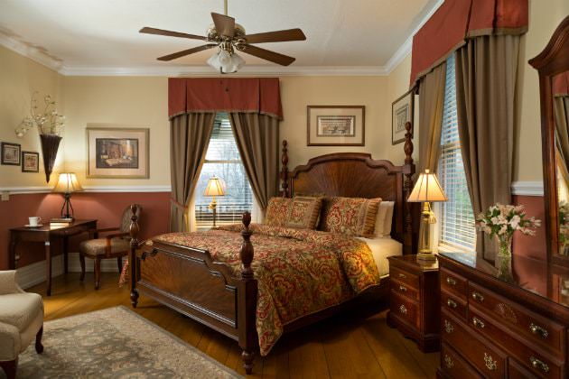 Creamy beige and rust red room with wood floors, elegant four poster bed, desk and chair and natural light