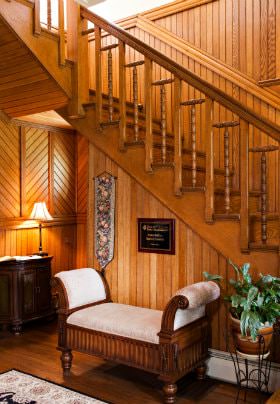 Wood paneled room, open L-shaped stairway with wood railing, and upholstered bench under the stairs