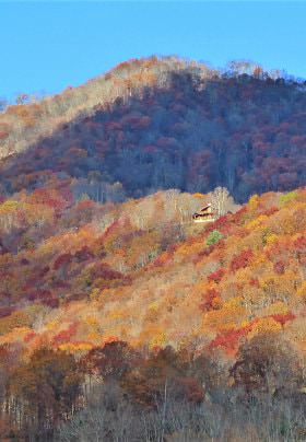 Mountain view with fading colored trees in red, orange and brown amidst blue skies