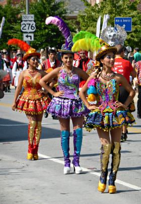 Parade with several women walking down the road wearing brightly colored costumes