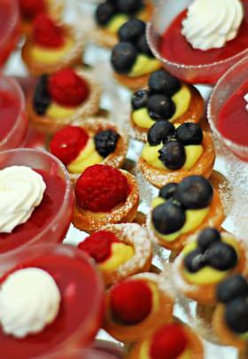 Rows of cups filled with red dessert and white whipped cream, and mini baked dessert cups topped with fresh fruit