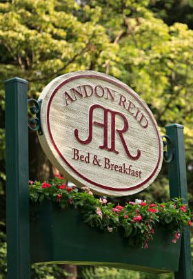 Green sign with flowerbox, colorful flowers and white oval sign with Andon Reid Bed & Breakfast in red lettering