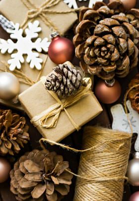 Pile of pinecones, white snowflakes, red and gold bulbs, and brown paper wrapped presents with burlap string