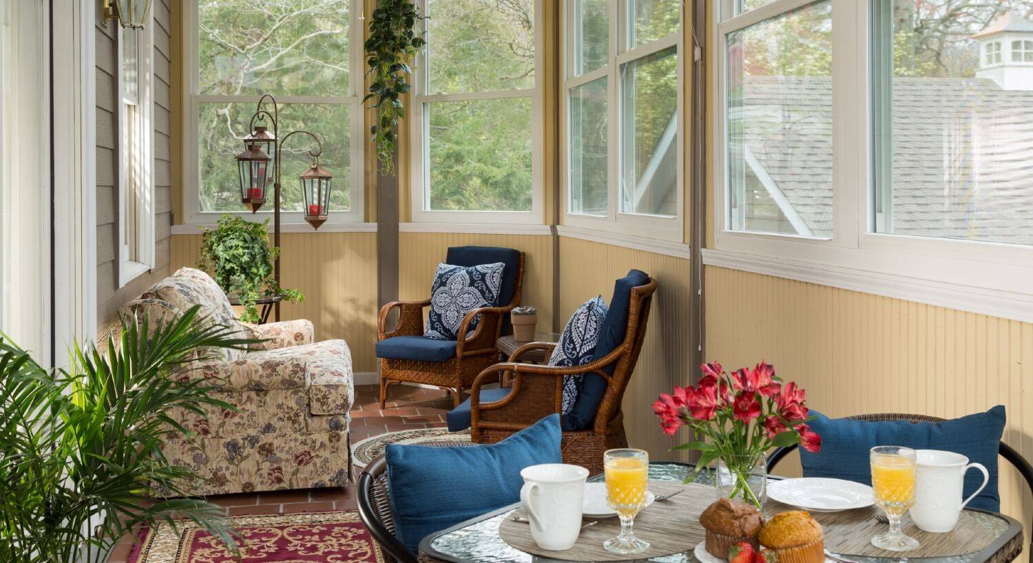 Sitting room surrounded by windows with three chairs and table set for two with muffins, coffee cups and glasses of orange juice