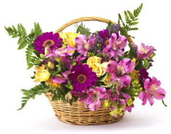 Tan wicker flower basket with handle filled with pink, violet and yellow flower with green leafy stems