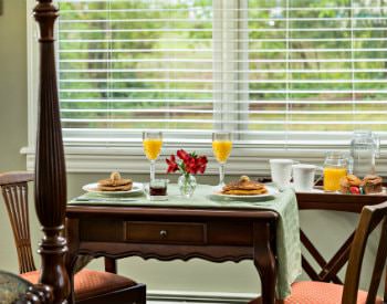 Small wood table with two chairs set for breakfast with pancakes and orange juice in front of double window