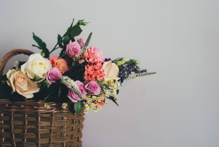 Brown basket full of an array of cream, peach, pink and purple flowers against a grey wall