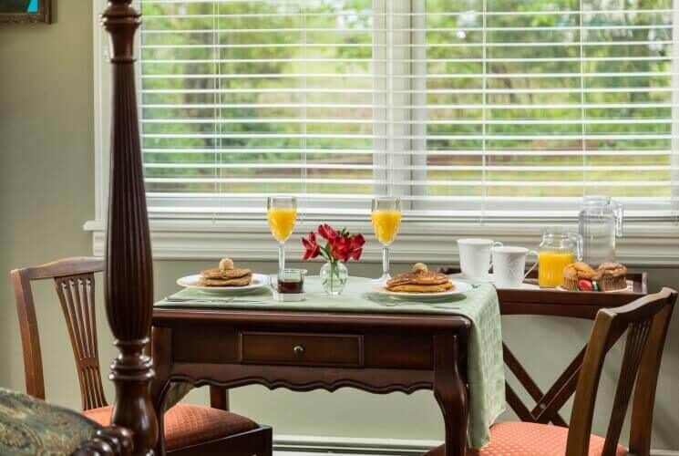 Table set for two with plates of pancakes, glasses of orange juice and side tray with coffee and muffins